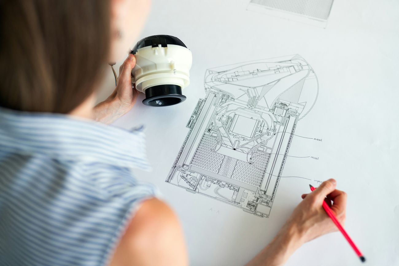 Engineer annotating a technical drawing while examining a physical component during a design review.